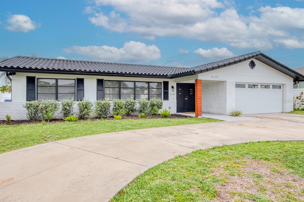 A single-story house with a white brick exterior, black roof tiles, and a circular driveway — 12125 6TH STREET E, TREASURE ISLAND, FL