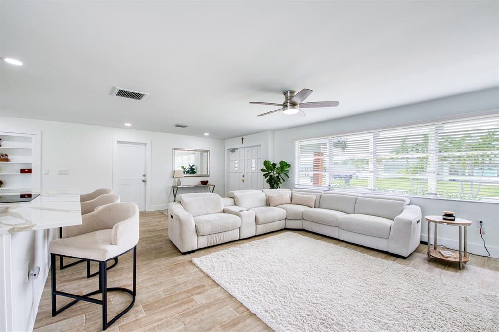 A bright living room features a white sectional sofa, tile floors, and a kitchen island — 12125 6TH STREET E, TREASURE ISLAND, FL
