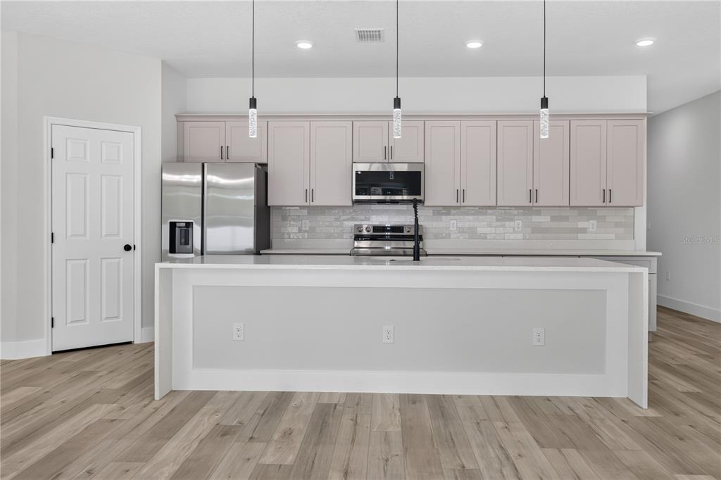 A modern kitchen features light gray cabinets, stainless steel appliances, and a large white island — 867 CORNELIA AVENUE SE, PALM BAY, FL