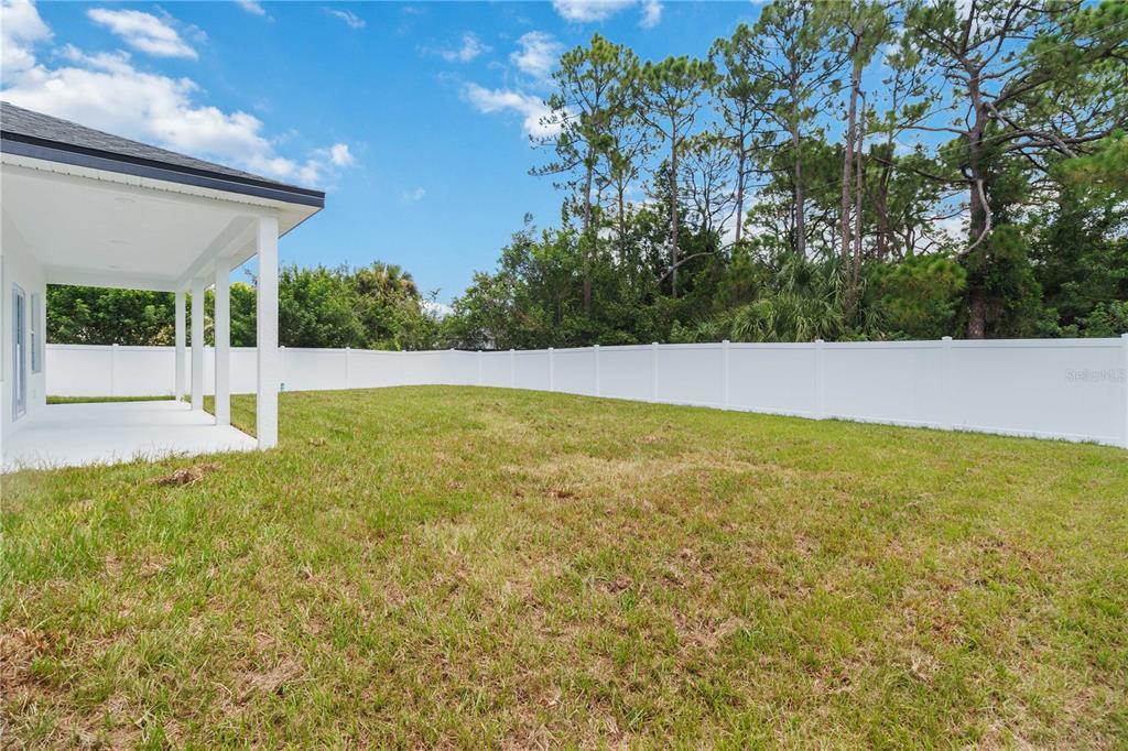 A backyard with a covered patio, green lawn, and a white vinyl privacy fence — 867 CORNELIA AVENUE SE, PALM BAY, FL