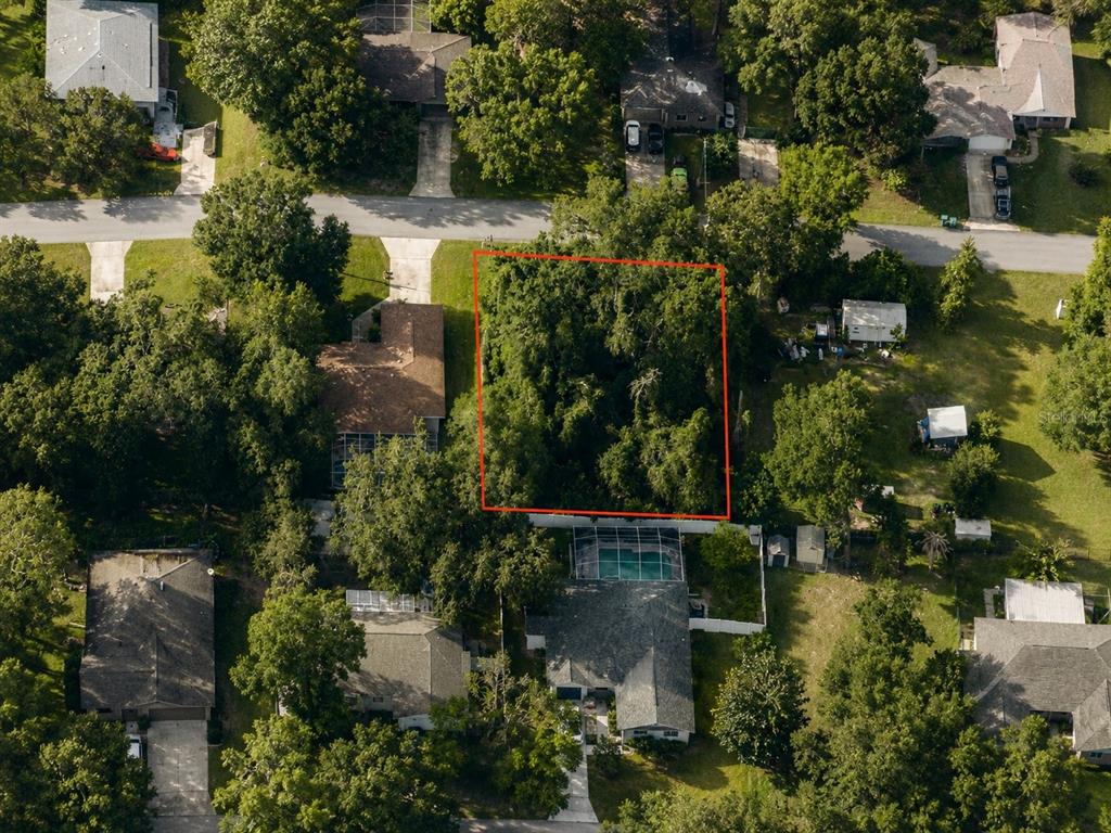 An aerial view shows a rectangular, tree-covered vacant lot outlined in red between residential homes — 6824 E FALCON REST LN, INVERNESS, FL