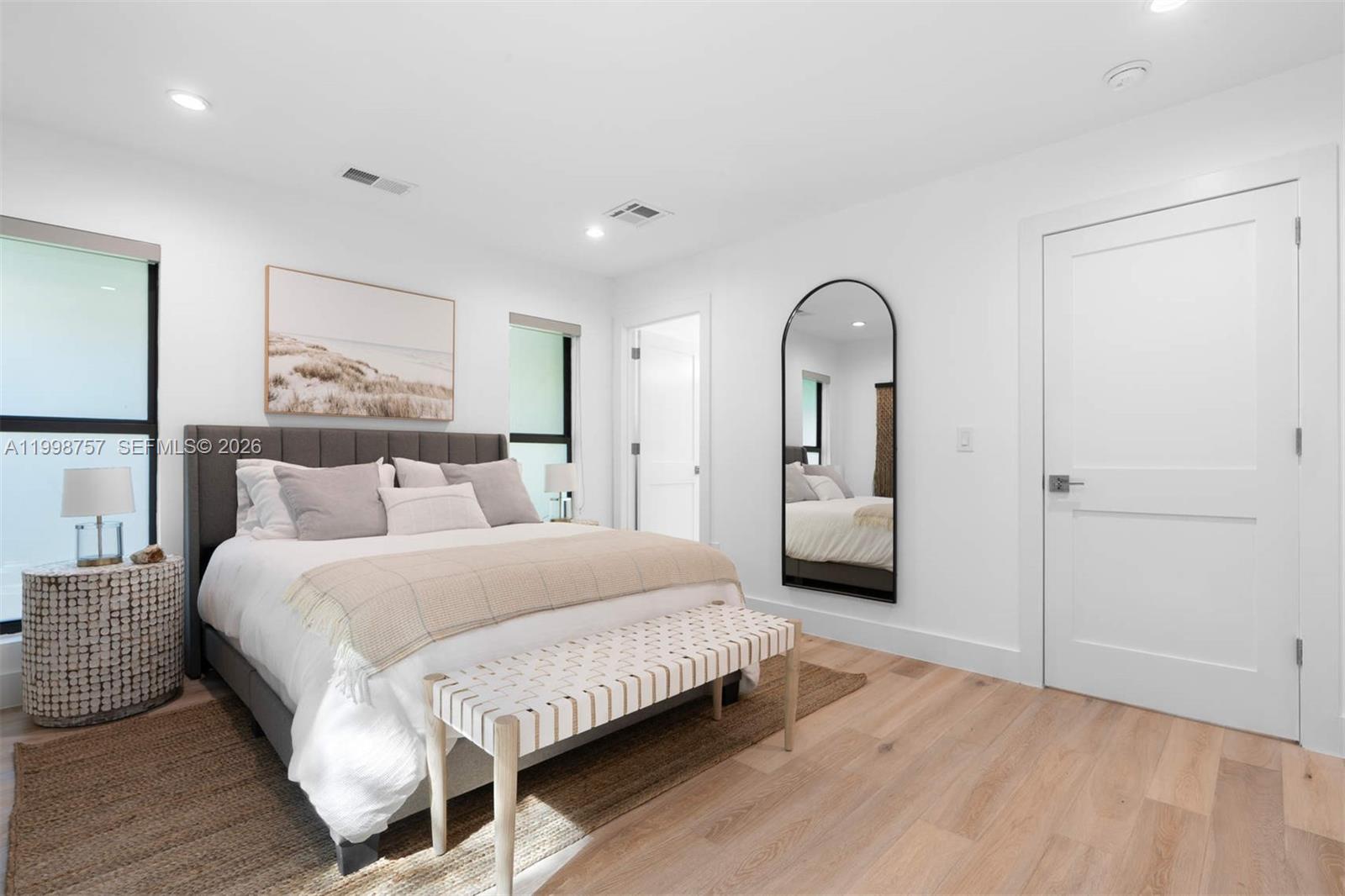 A bedroom features a bed with a gray headboard, a floor mirror, and light wood flooring — 18 Hersey Dr, Ocean Ridge FL 33435, OCEAN RIDGE, FL