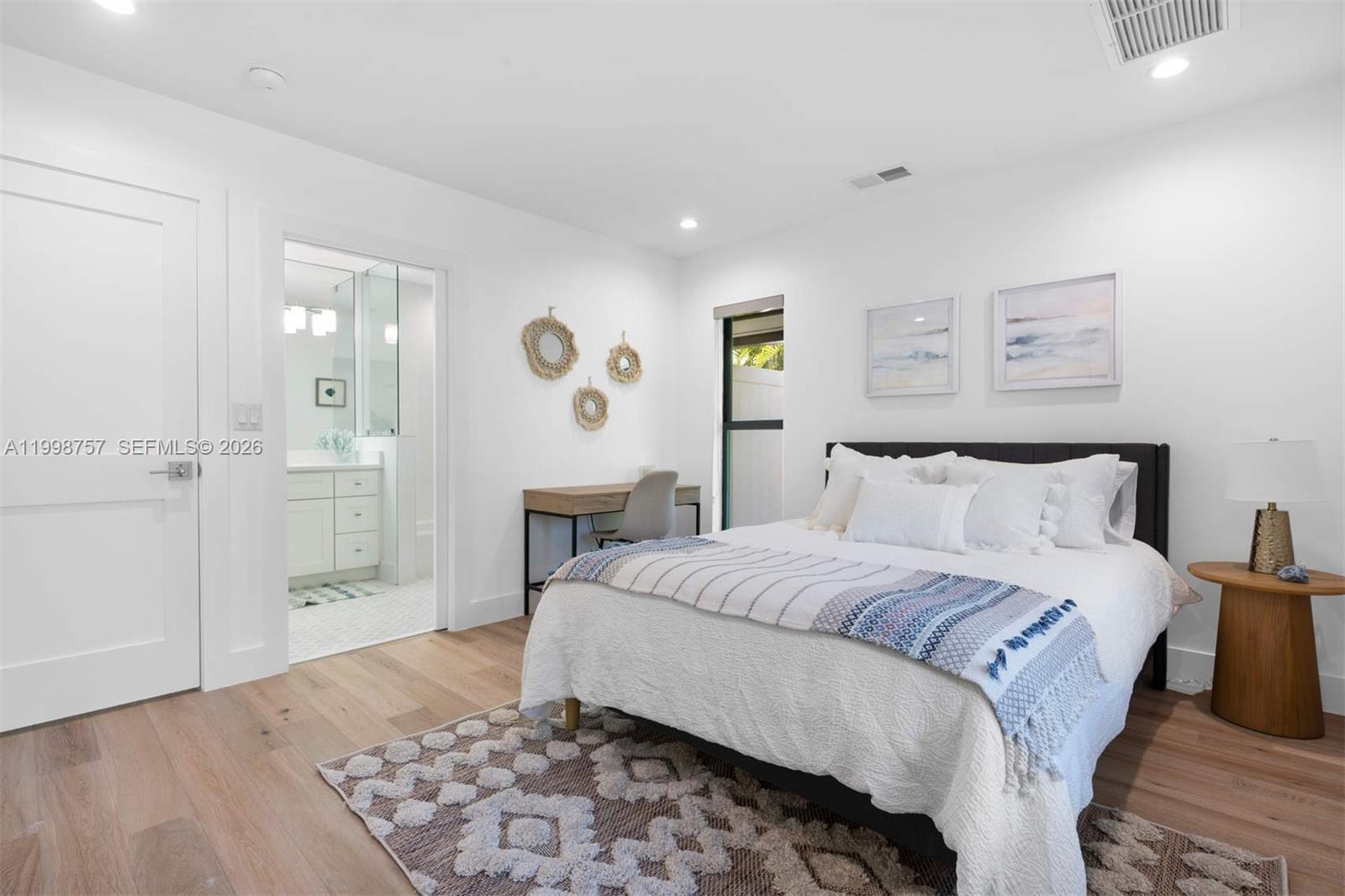 A bright bedroom features a bed, a desk, and an attached bathroom with white finishes — 18 Hersey Dr, Ocean Ridge FL 33435, OCEAN RIDGE, FL
