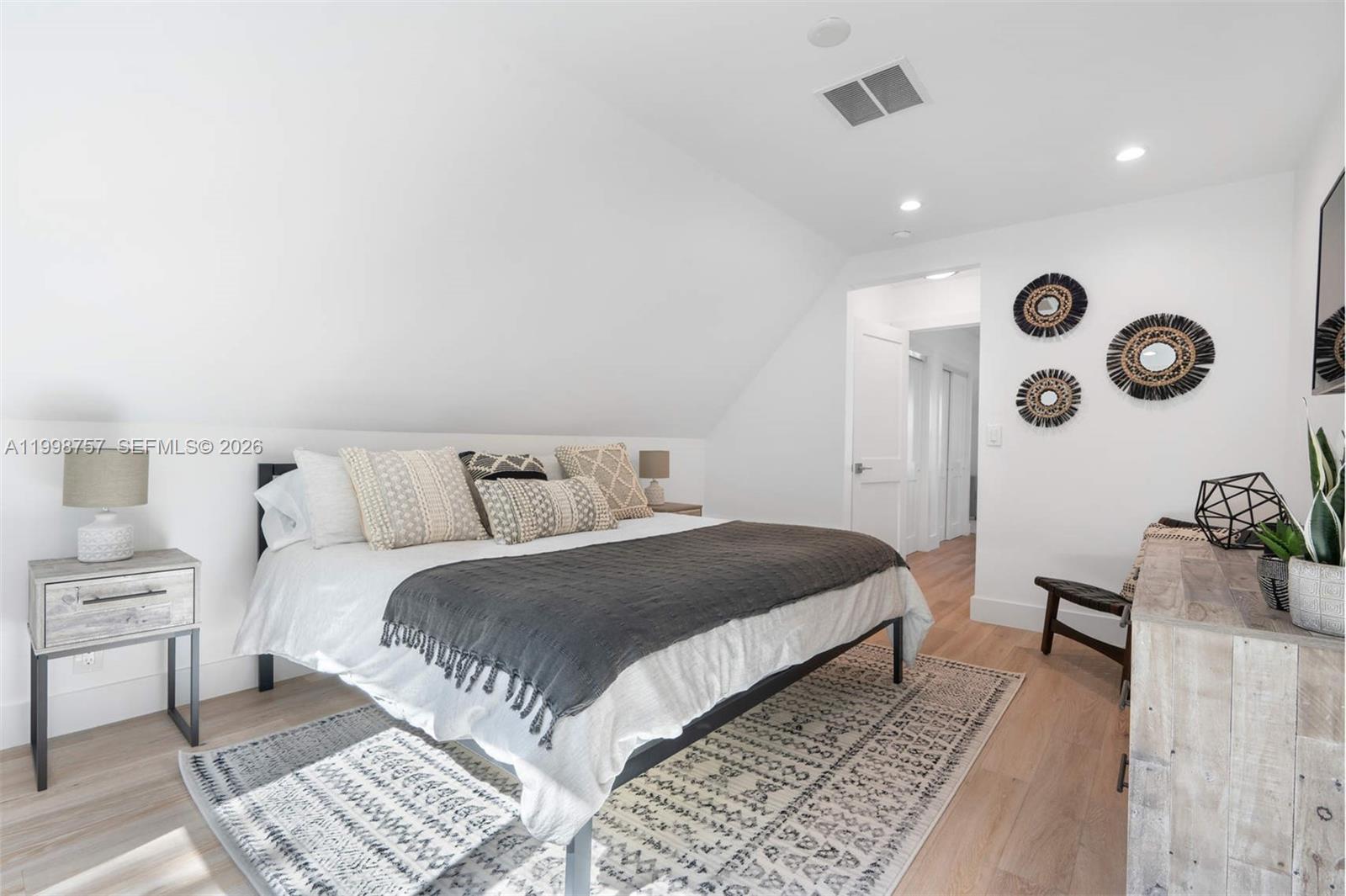 A bedroom features a bed with a sloped ceiling, light wood floors, and neutral decor — 18 Hersey Dr, Ocean Ridge FL 33435, OCEAN RIDGE, FL