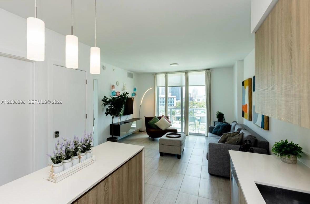 A modern living room and kitchen area with light tile floors and a balcony view — 3900 Biscayne Blvd # 906, Miami FL 33137, MIAMI, FL