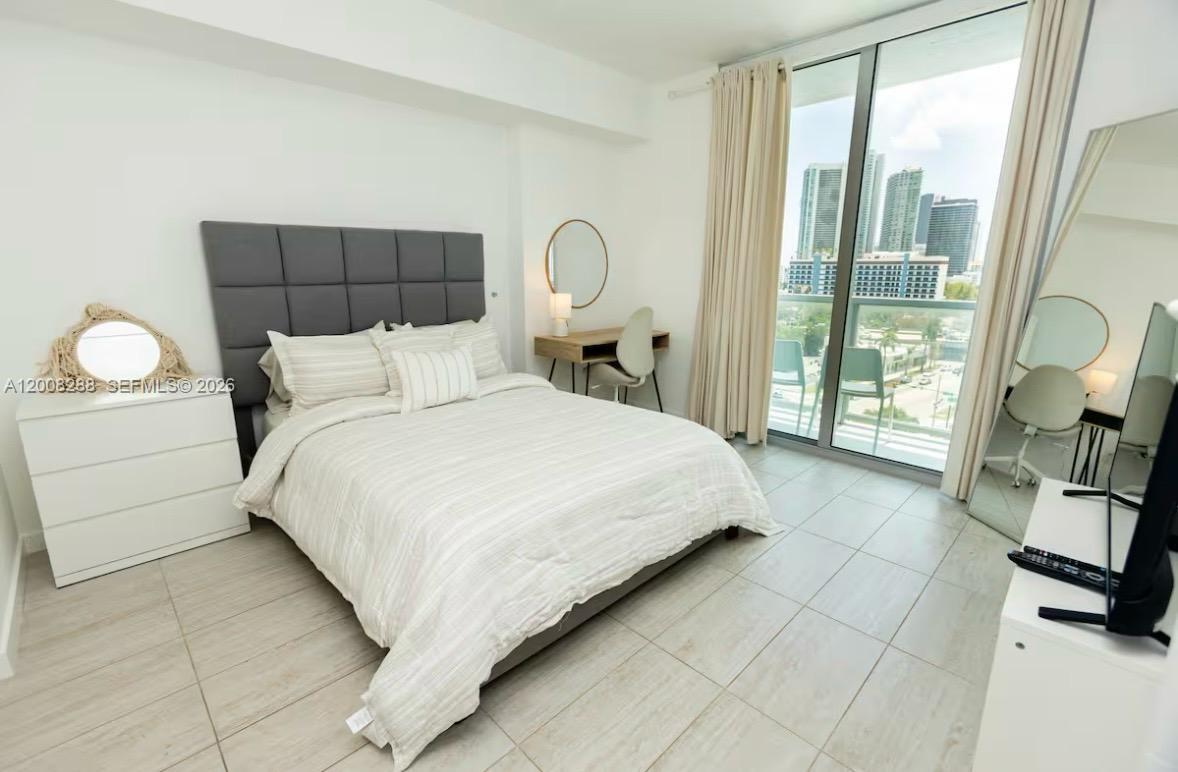 A bedroom features a queen bed, a desk, a large mirror, and floor-to-ceiling windows — 3900 Biscayne Blvd # 906, Miami FL 33137, MIAMI, FL