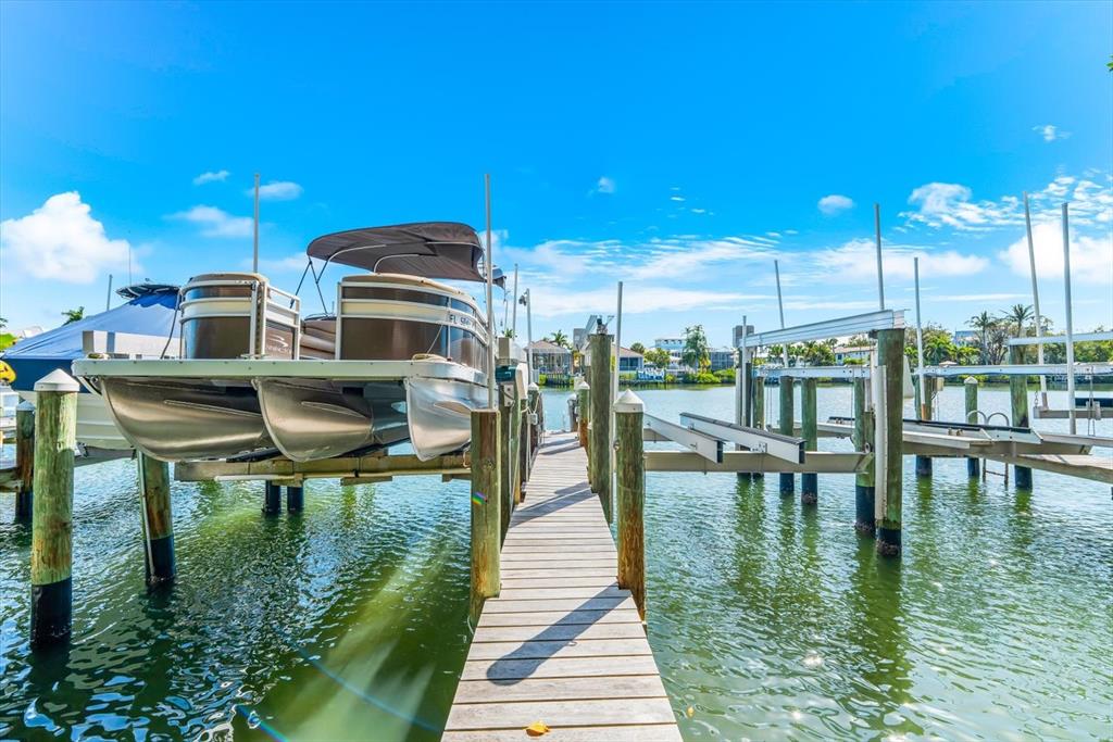 A wooden dock leads to boat lifts holding a pontoon boat over calm water — 3941 HAMILTON CLUB CIRCLE UNIT 9, SARASOTA, FL