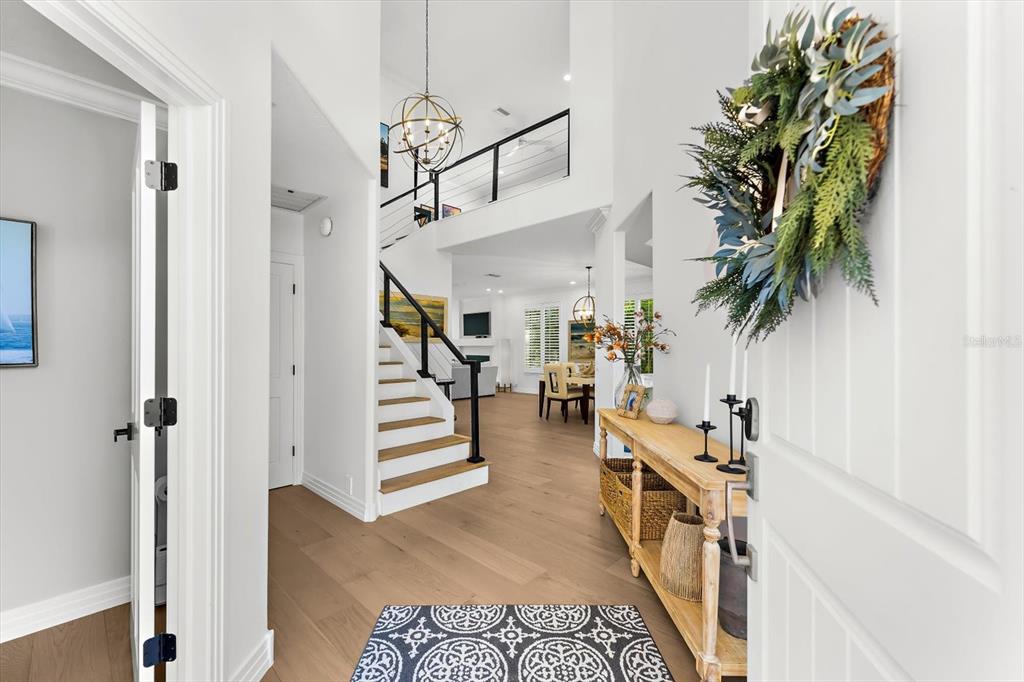 A bright entryway features light wood floors, a staircase with black railings, and a console table — 3941 HAMILTON CLUB CIRCLE UNIT 9, SARASOTA, FL