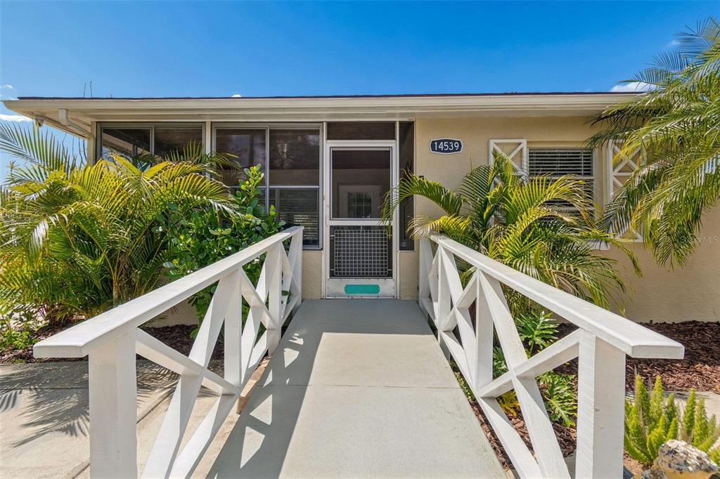A concrete ramp with white lattice railings leads to the screened front entrance of a house — 14539 COFFEY LANE, HUDSON, FL