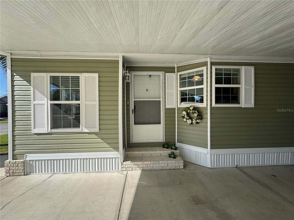 The exterior of a house features olive green siding, white shutters, and a concrete carport — 6394 LOLLY BAY LOOP NE, WINTER HAVEN, FL