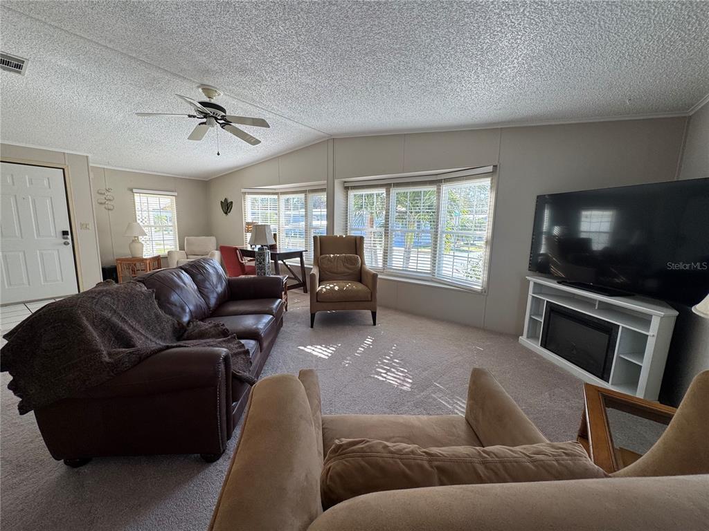 A living room features a brown leather sofa, tan armchairs, a television, and carpeted floors — 6394 LOLLY BAY LOOP NE, WINTER HAVEN, FL