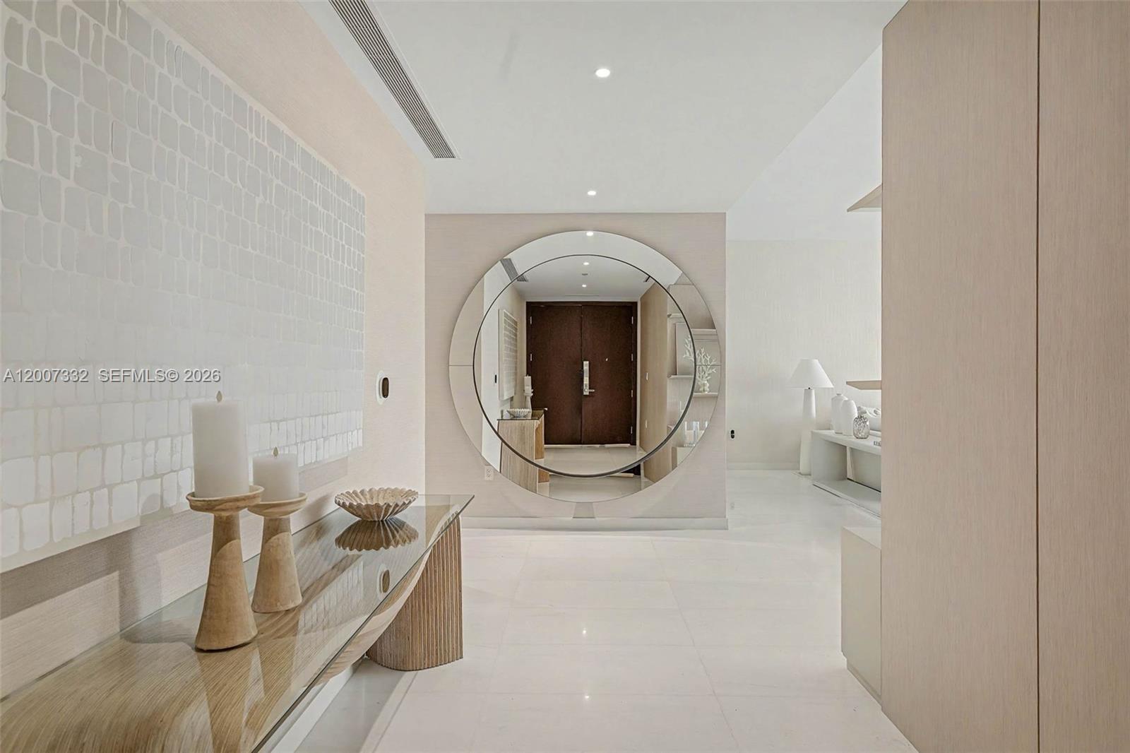 A modern entryway features a large circular mirror, a glass console table, and light-colored flooring — 300 Biscayne Blvd Way # 3203, Miami FL 33131, MIAMI, FL