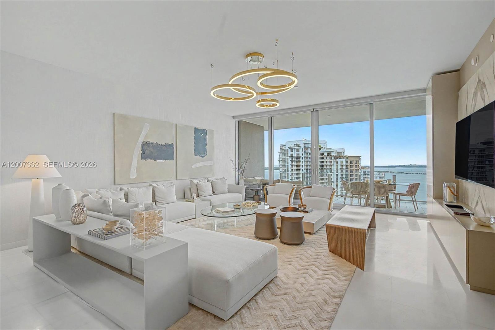 A modern living room features a large white sectional, circular chandelier, and floor-to-ceiling balcony windows — 300 Biscayne Blvd Way # 3203, Miami FL 33131, MIAMI, FL