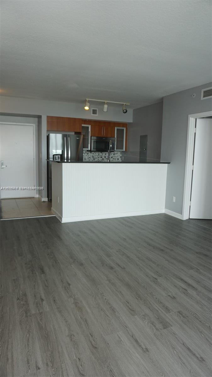 A kitchen with wood cabinets and a breakfast bar overlooks a room with gray flooring — 325 S Biscayne Blvd # 2022, Miami FL 33131, MIAMI, FL