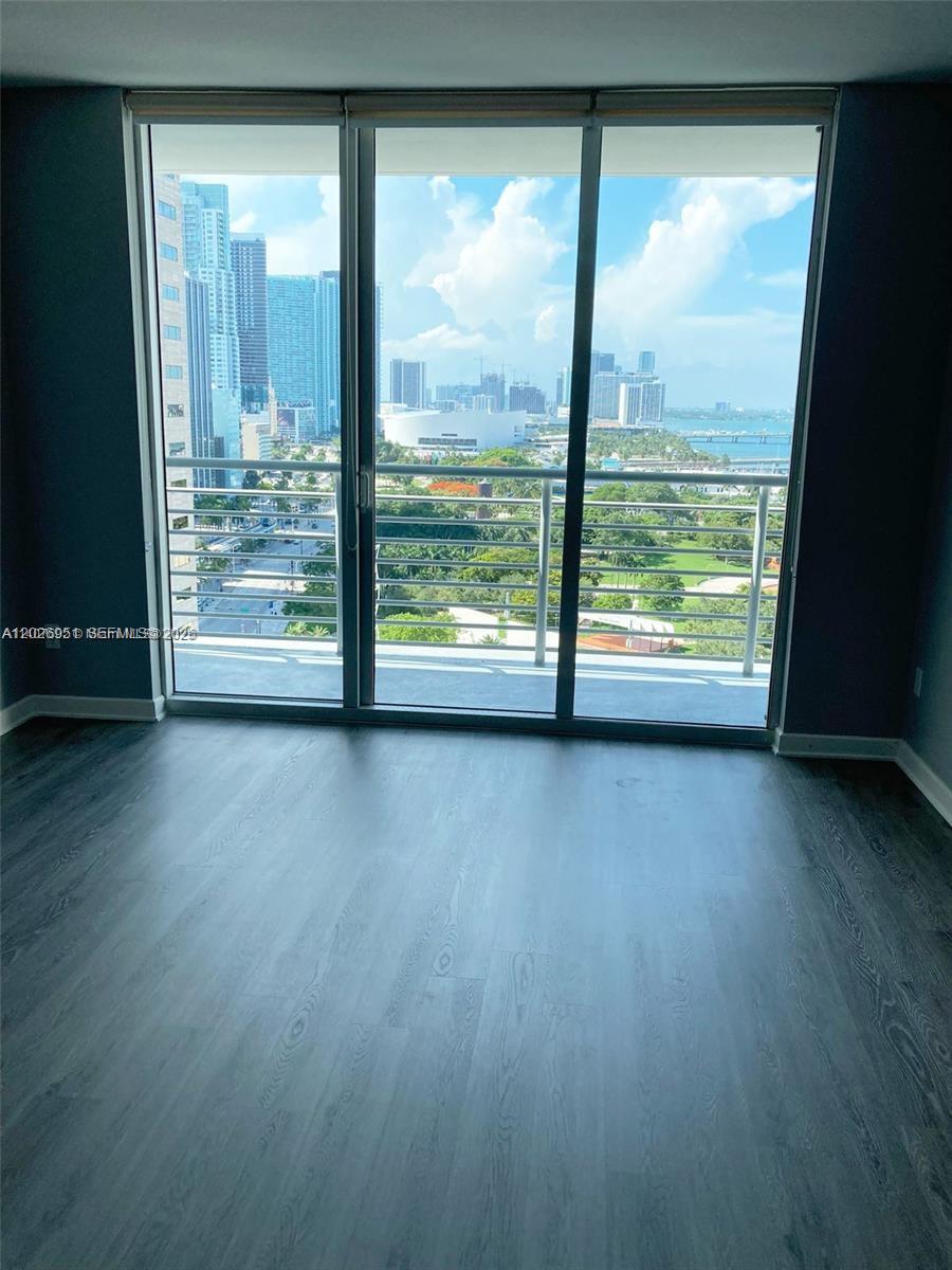 A room with gray wood-look flooring features a large sliding glass door overlooking a city — 325 S Biscayne Blvd # 2022, Miami FL 33131, MIAMI, FL