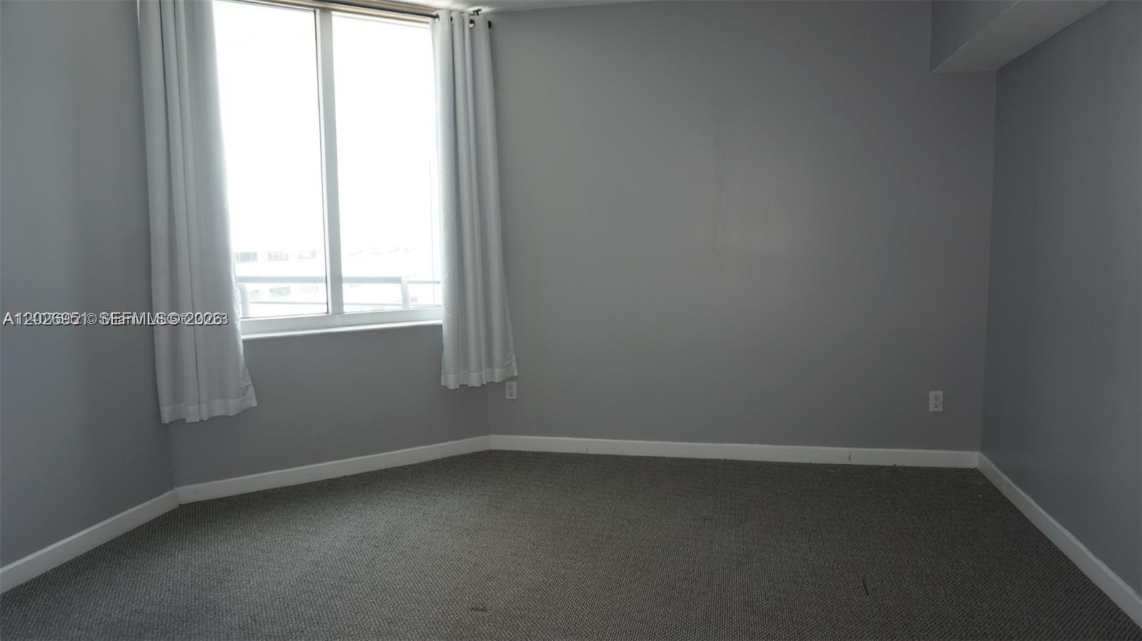 An empty room features gray walls, gray carpeting, and a window with white curtains — 325 S Biscayne Blvd # 2022, Miami FL 33131, MIAMI, FL