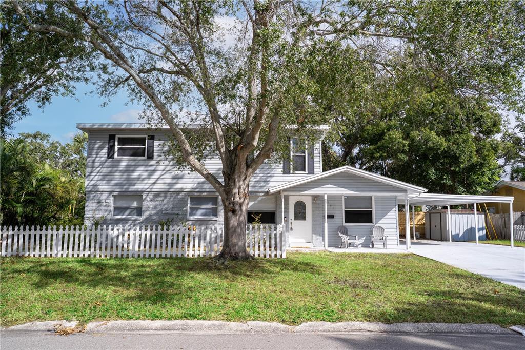 A two-story house with light gray siding, a white picket fence, and a carport — 7991 24TH AVE N AVENUE N, ST PETERSBURG, FL