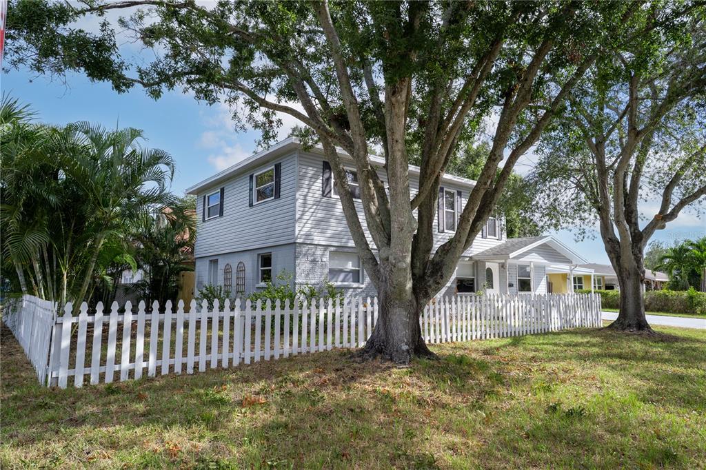 A two-story house with light gray siding and a white picket fence under large trees — 7991 24TH AVE N AVENUE N, ST PETERSBURG, FL