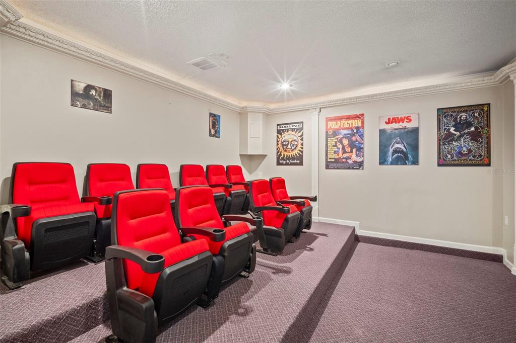 A home theater room features tiered rows of red cinema seats and movie posters — 3884 GOSHAWK PLACE, TITUSVILLE, FL