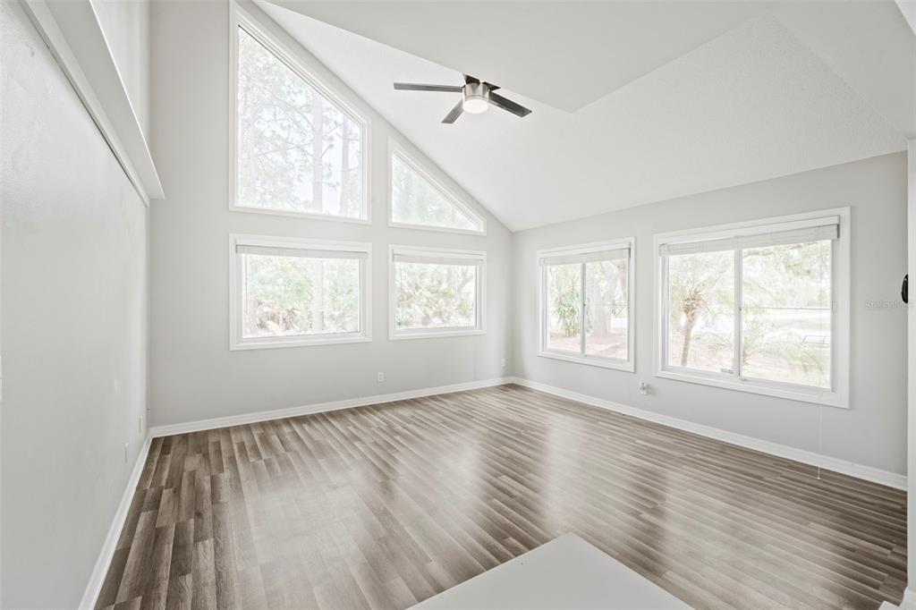 An empty room with light gray walls, wood-look flooring, vaulted ceilings, and multiple windows — 3884 GOSHAWK PLACE, TITUSVILLE, FL