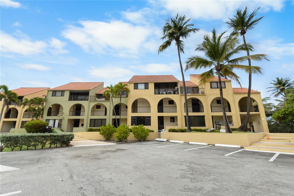 A multi-story tan apartment building features arched entryways, balconies, and a paved parking lot — 94 BEACH VILLAGE DRIVE UNIT 94, HUMACAO, PR