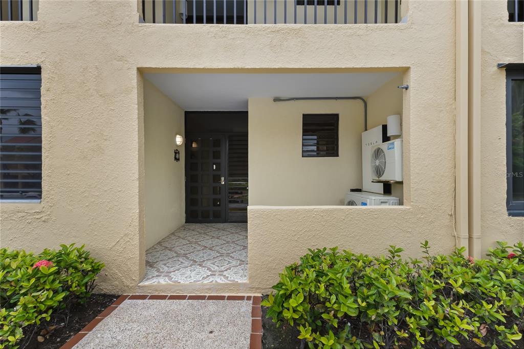 A ground-level apartment entrance features a tiled porch, a dark door, and an exterior AC unit — 94 BEACH VILLAGE DRIVE UNIT 94, HUMACAO, PR