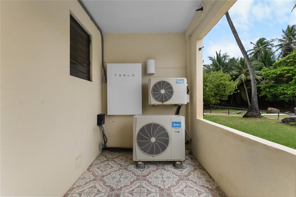 A patio features two Midea air conditioning units and a Tesla Powerwall mounted on a wall — 94 BEACH VILLAGE DRIVE UNIT 94, HUMACAO, PR