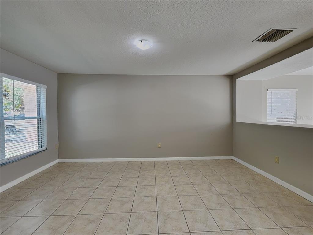 An empty room features beige walls, light-colored tile flooring, a window, and a pass-through opening — 10432 BOYETTE CREEK BOULEVARD, RIVERVIEW, FL