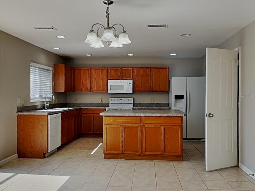 A kitchen features wood cabinets, a central island, white appliances, and light-colored tile flooring — 10432 BOYETTE CREEK BOULEVARD, RIVERVIEW, FL