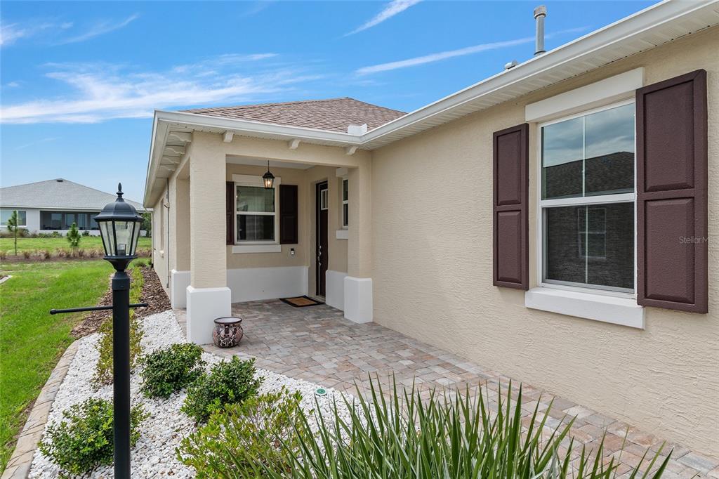 A beige stucco house features a covered entryway with a paver porch and brown shutters — 9722 SW 102ND TERRACE, OCALA, FL