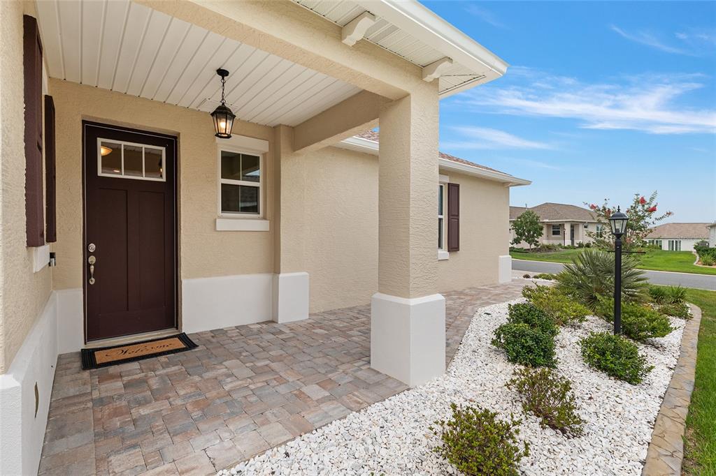 A beige house exterior features a covered entryway with a paver porch and dark door — 9722 SW 102ND TERRACE, OCALA, FL