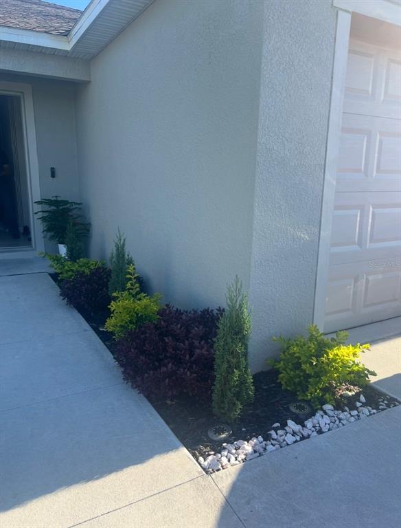 A landscaped garden bed with shrubs and small evergreens sits beside a concrete walkway — 360 TOWNS CIRCLE, HAINES CITY, FL