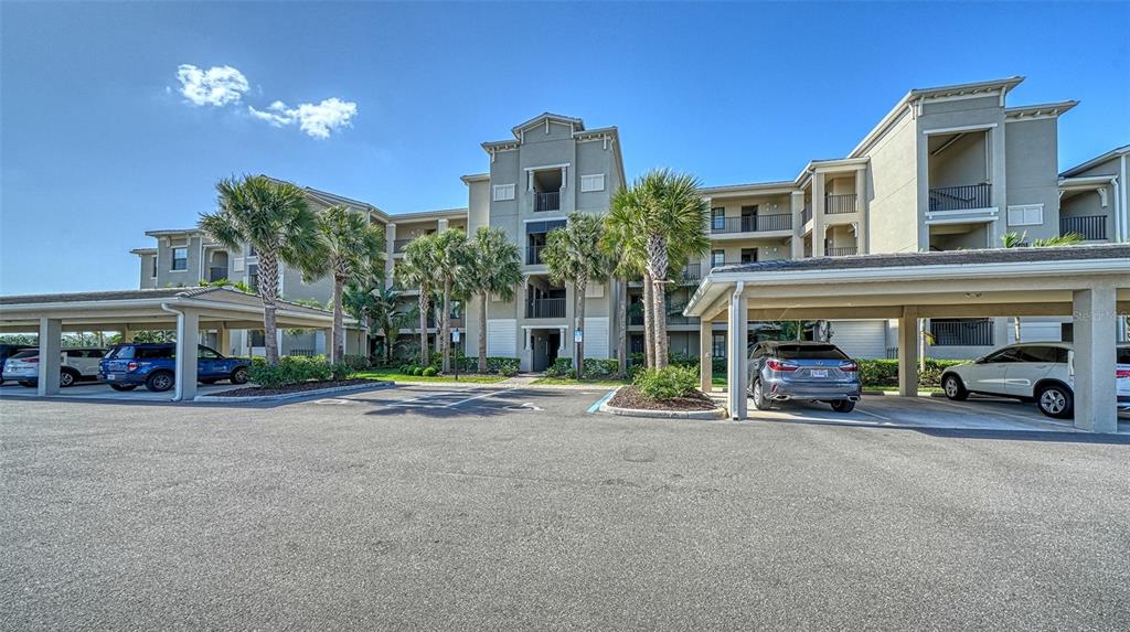 A multi-story apartment building with covered parking spaces and palm trees in the foreground — 18114 GAWTHROP DRIVE UNIT 308, LAKEWOOD RANCH, FL