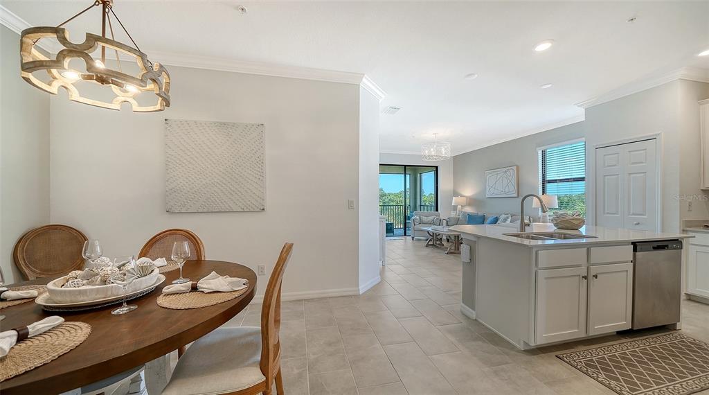 A dining area with a wooden table opens into a kitchen and living room space — 18114 GAWTHROP DRIVE UNIT 308, LAKEWOOD RANCH, FL