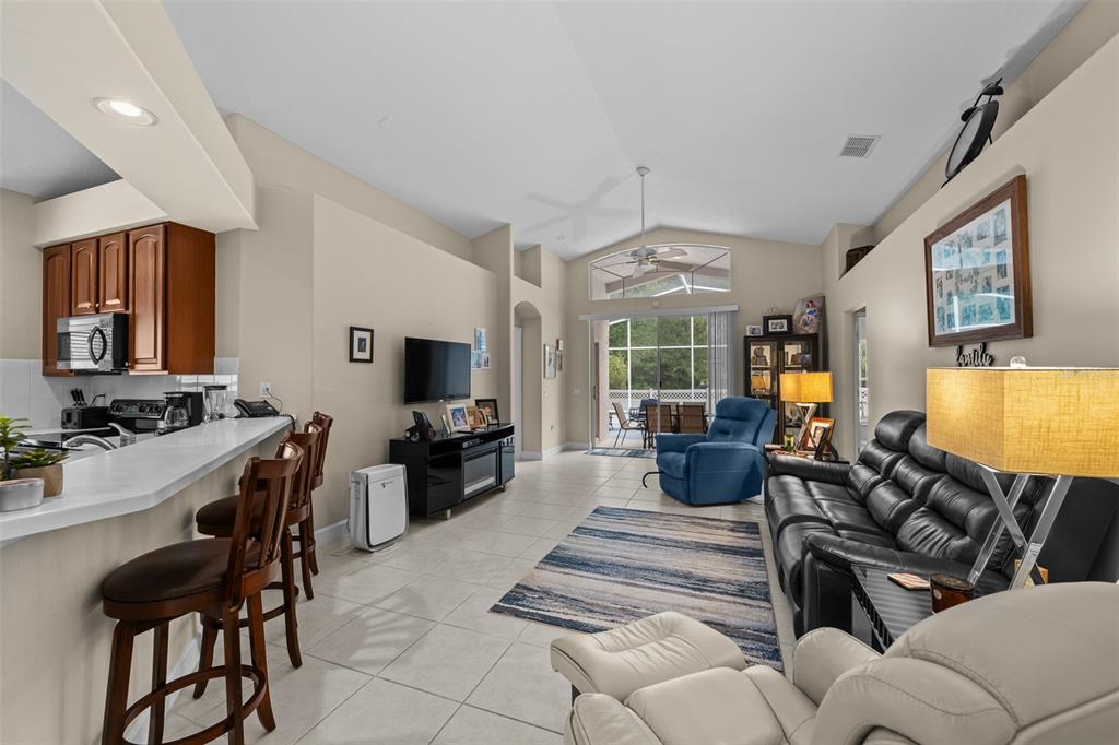 An open-concept living room features a kitchen breakfast bar, tile flooring, and vaulted ceilings — 16230 NOTTINGHAM PARKWAY, TAMPA, FL