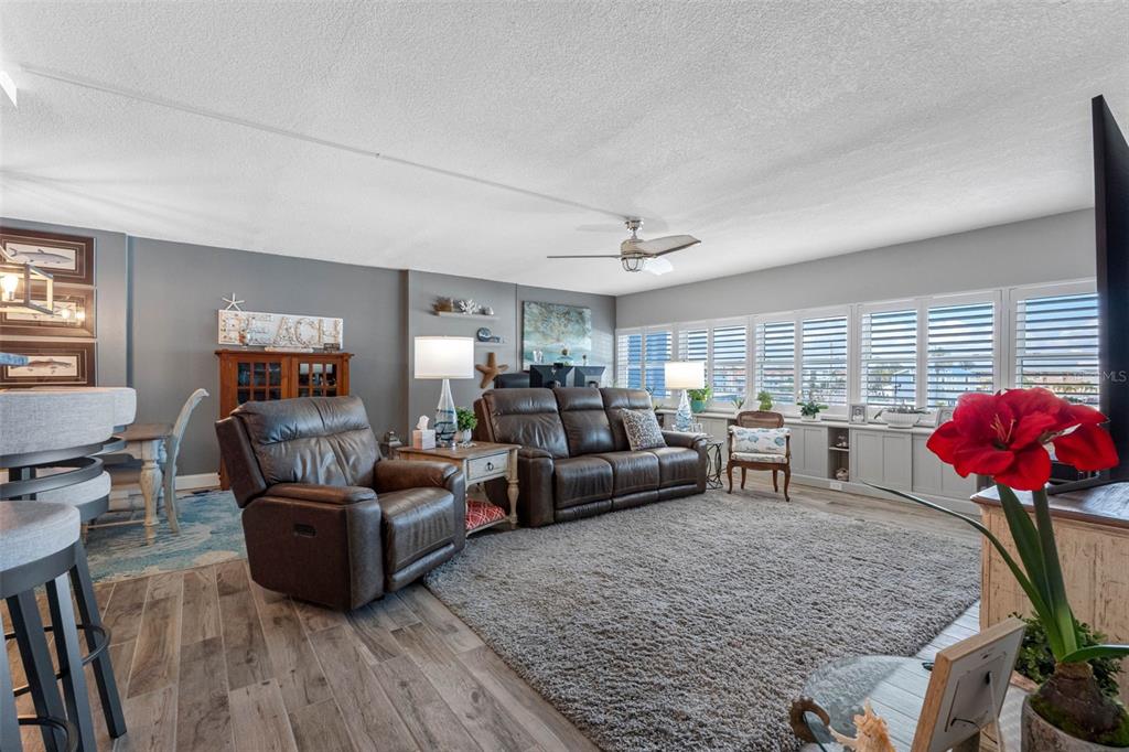 A living room features a brown leather sofa, recliner, gray area rug, and plantation shutters — 17400 GULF BOULEVARD UNIT I3, REDINGTON SHORES, FL