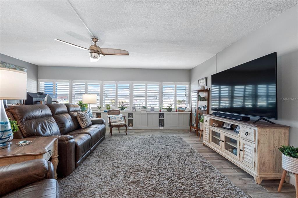 A living room features a brown leather sofa, a large television, and white window shutters — 17400 GULF BOULEVARD UNIT I3, REDINGTON SHORES, FL