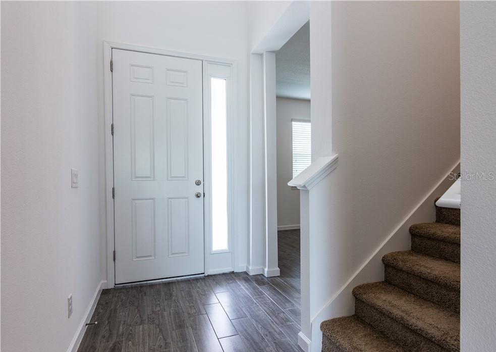 An entryway features a white front door, wood-look tile flooring, and a carpeted staircase — 7591 TANGERINE KNOLL LOOP, WINTER GARDEN, FL
