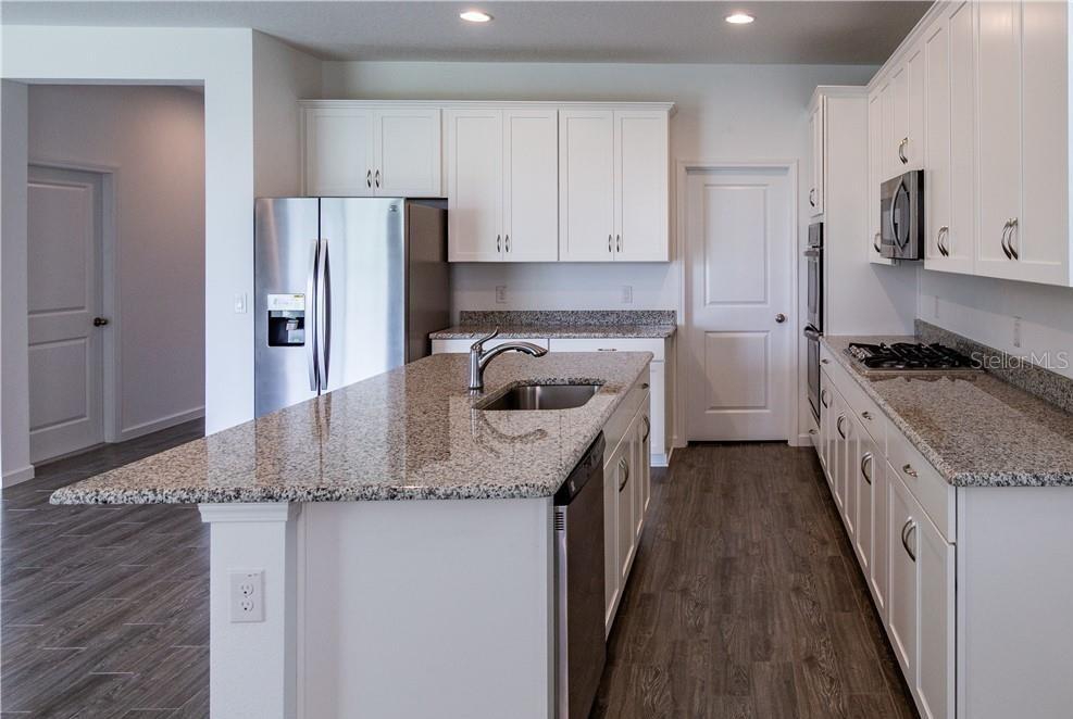A kitchen features white cabinets, granite countertops, stainless steel appliances, and a central island — 7591 TANGERINE KNOLL LOOP, WINTER GARDEN, FL