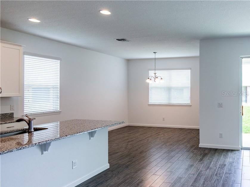 A kitchen island with granite countertops overlooks an open dining area with wood-look flooring — 7591 TANGERINE KNOLL LOOP, WINTER GARDEN, FL