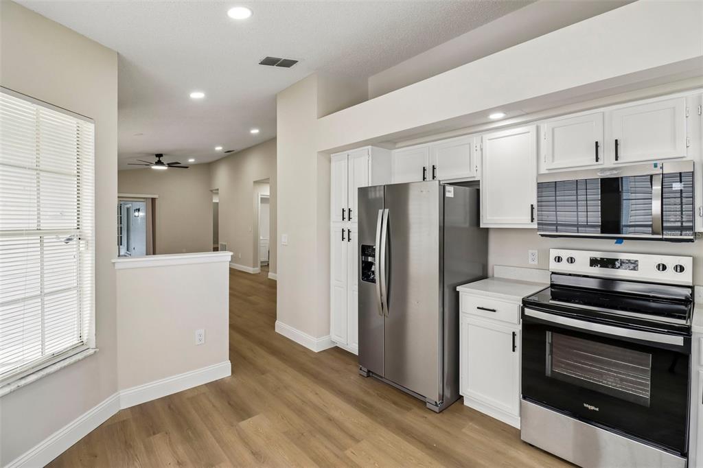 A kitchen with white cabinets, stainless steel appliances, and light wood-look flooring — 106 LAMPLIGHTER DRIVE, SANFORD, FL