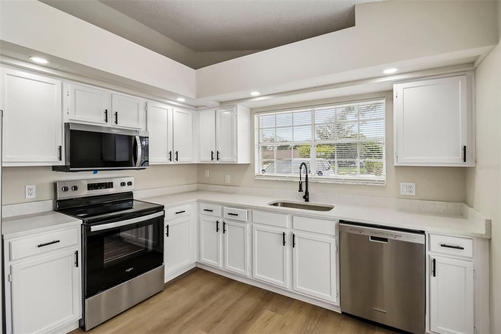 A kitchen with white cabinets, stainless steel appliances, light countertops, and wood-look flooring — 106 LAMPLIGHTER DRIVE, SANFORD, FL