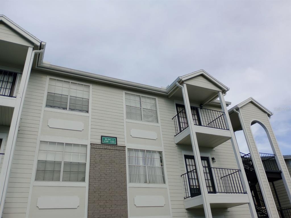 A low-angle view of a multi-story apartment building exterior with light siding and brick accents — 2550 N ALAFAYA TRAIL UNIT 4305, ORLANDO, FL