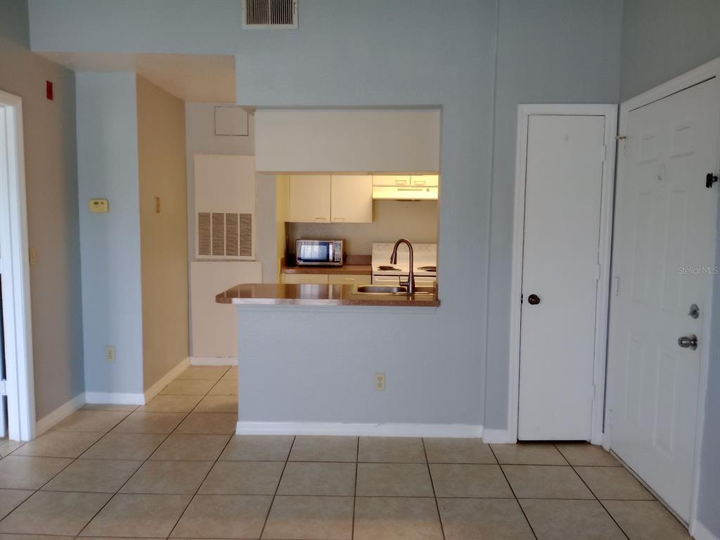 A kitchen with a breakfast bar, light-colored cabinets, and tile flooring opens to a living area — 2550 N ALAFAYA TRAIL UNIT 4305, ORLANDO, FL