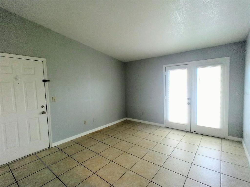 An empty room features light gray walls, beige tile flooring, a white door, and glass doors — 2550 N ALAFAYA TRAIL UNIT 4305, ORLANDO, FL