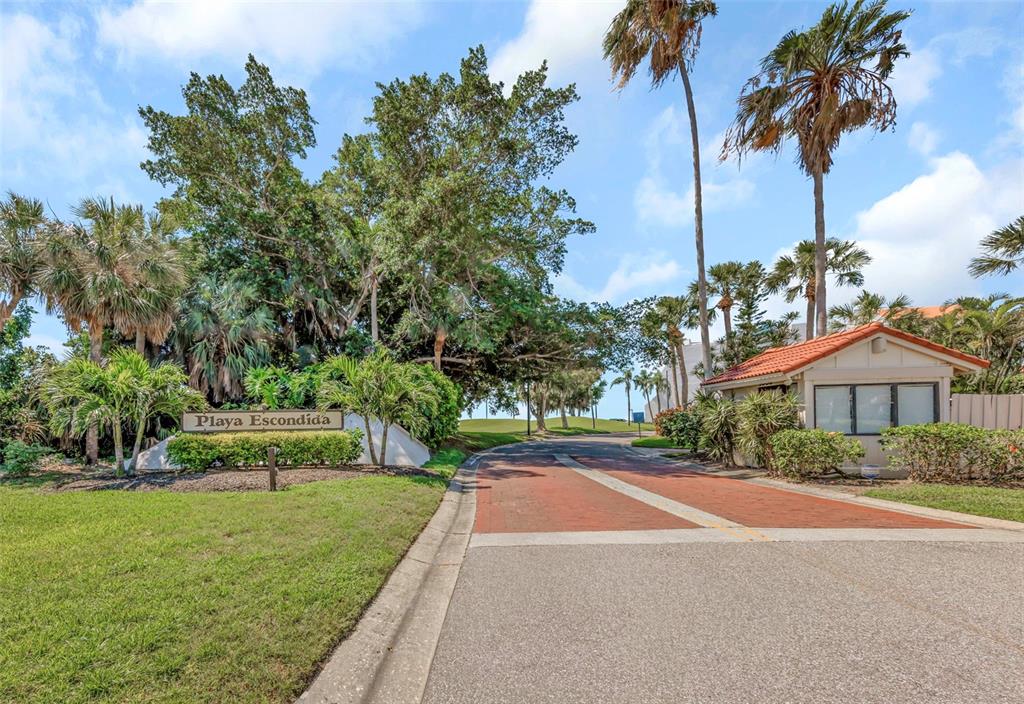 A brick-paved entrance road leads to a gated community sign labeled Playa Escondida — 5650 ESCONDIDA BOULEVARD S, ST PETERSBURG, FL