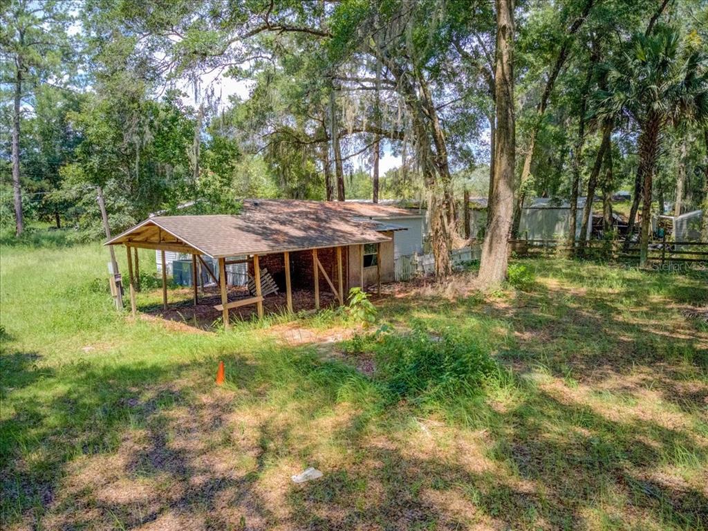 A small house with a wooden carport sits on a grassy, tree-filled lot — 5530 SE 41ST ST OCALA ,FL, OCALA, FL