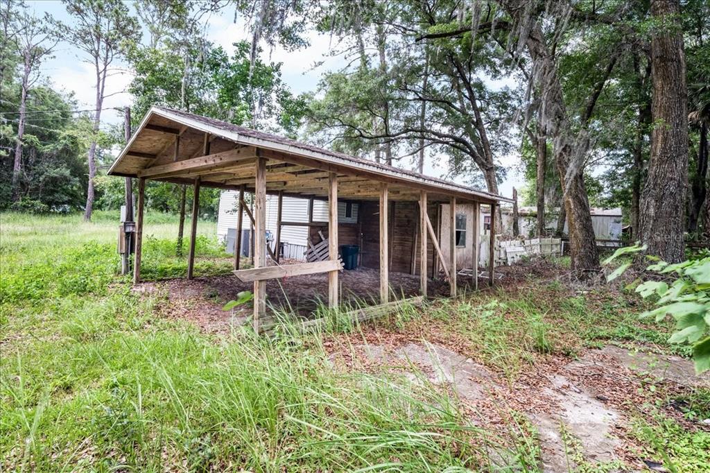 An open-sided wooden carport stands in a grassy, wooded lot next to a mobile home — 5530 SE 41ST ST OCALA ,FL, OCALA, FL