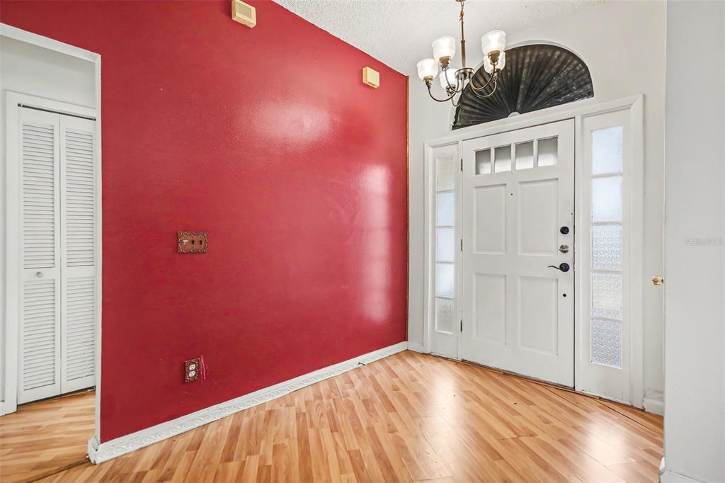 An entryway features a red accent wall, wood-look flooring, a chandelier, and a white door — 2058 SUE ELLEN COURT, APOPKA, FL