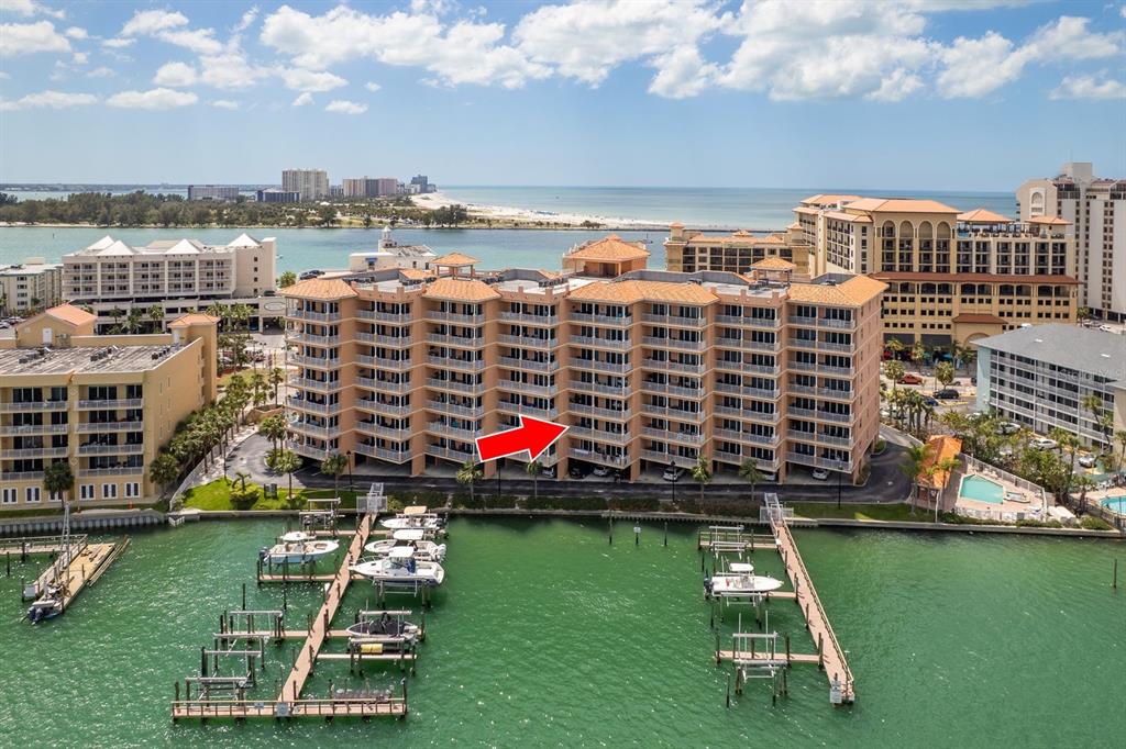 An aerial view shows a multi-story waterfront condominium building with a red arrow pointing down — 530 S GULFVIEW BOULEVARD UNIT 303, CLEARWATER, FL